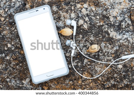Aerial view of white smart phone with white isolated screen and headphones on stone surface. Mockup. Copy space available.