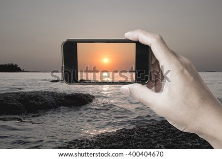 Hand take a photo of sunset on the beach by smart phone