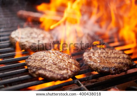 hamburgers and hot dogs cooking on grill with flames