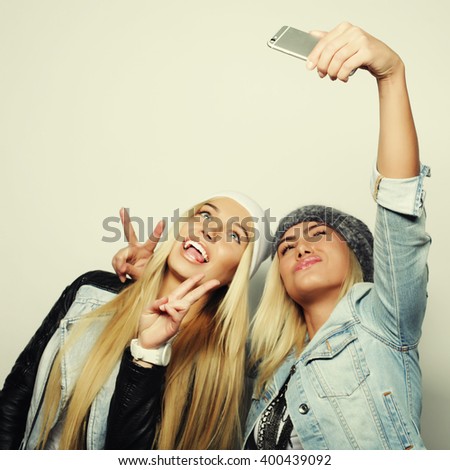 Two teenage girls friends in hipster outfit make selfie on a phone. 