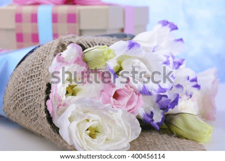 Beautiful Mother's Day lisianthus flowers wrapped in burlap and blue paper with gift box on white wood table and blue background, closeup.