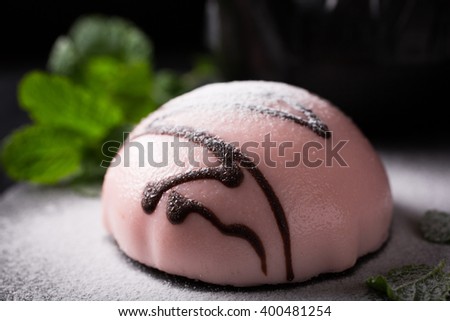 Individual mousse cake in the form of hemisphere covered with pink glaze with mint leaves on dark background. Holiday food concept with copy space for text.