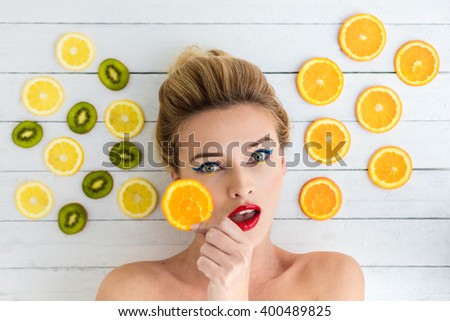 beautiful blonde woman laying on a white wooden table next to slices of orange, lemon and kiwi