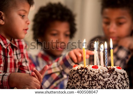 Black kid touching cake's candle. Boy touches birthday cake's candle. Be careful, my friend. Don't play with fire.