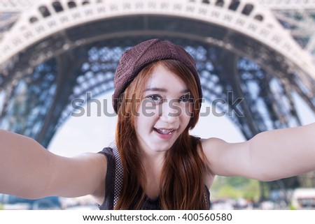 Happy teenage girl taking photo of herself with a camera at Eiffel Tower