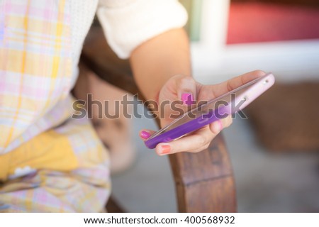 Young hipster woman holding smartphone on her left hand while sitting on wood bench in morning time