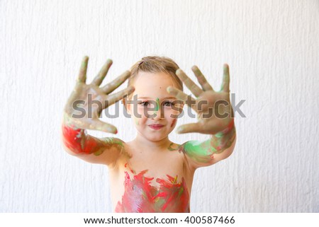 Little girl showing her hands, covered in finger paint after painting a picture and her body with it. Playfulness, creativity, permissive parenting, fun childhood concept, selective sharpness. 