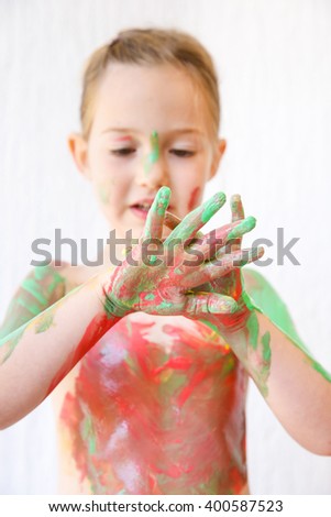 Little girl with hands covered in finger paint after painting a picture and her body with it. Tactile play, innovative learning, permissive upbringing, fun childhood concept, blur.