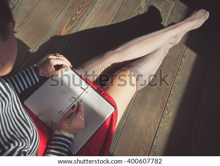Cozy photo of young woman writing in notebook sitting on the floor in sunlight