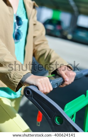 Young woman holding shopping push cart closeup picture of hands with car on background
