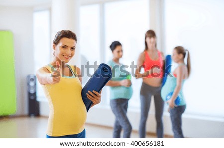 pregnancy, sport, fitness, people and healthy lifestyle concept - happy pregnant woman with mat in gym showing thumbs up 