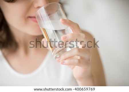 Happy beautiful young woman drinking water. Smiling caucasian female model holding transparent glass in her hand. Closeup. Focus on the arm Royalty-Free Stock Photo #400659769
