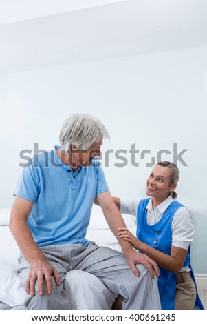 Smiling nurse comforting senior man at bed in hospital