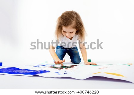 Adorable little girl, modern hair style, white shirt, blue jeans is drawing pictures by her hands with paints. Isolate.