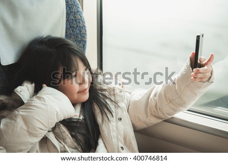 Little asian girl taking selfie picture  and sharing social media in a smart phone . She travels on a train