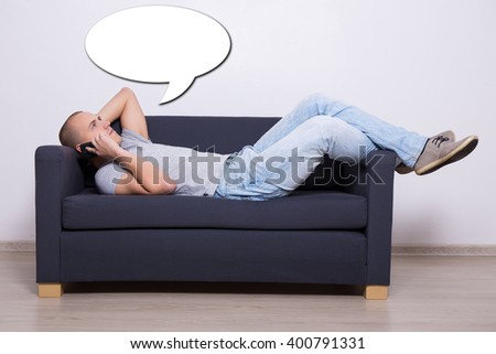 young man lying on sofa and talking on mobile phone at home and white speech bubble