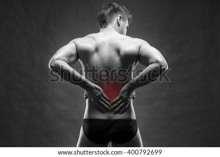 Kidney pain. Man with backache. Handsome muscular bodybuilder posing on gray background. Black and white photo with red dot