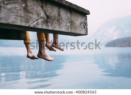 Father and son swung their legs from the wooden pier on mountain lake Royalty-Free Stock Photo #400824565