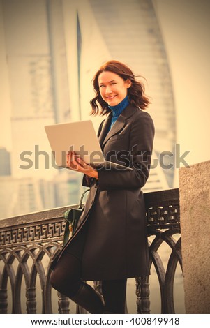 beautiful woman in a dark coat with a laptop at outdoors. instagram image filter retro style