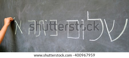 Young child hand writes Hello First Grade greetings in Hebrew (Shalom Kita Alef) on a chalkboard in Israeli primary school at the beginning of the school year. Education concept photo.  Copy Space