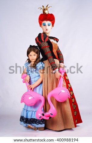Portrait girl in costume Red Queen and little girl Alice in a blue dress with flamingo in hands 