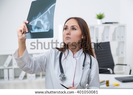 Female doctor standing at table and looking at X-rays. Light background. Concept of work.