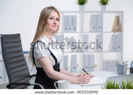 Businesswoman at table making notes. Side view. Shelves at background. Concept of work.