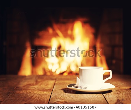 White cup of tea with teabag on wooden table near  fireplace. Winter and Christmas holiday concept. Photo with retro filter effect. Royalty-Free Stock Photo #401051587