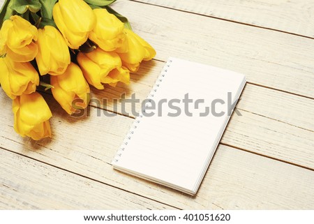 Fresh yellow tulips with greeting card on wooden background. Top view with copy space. Photo with retro filter effect.
