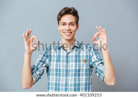 Smiling casual man showing ok sign with fingers over gray background