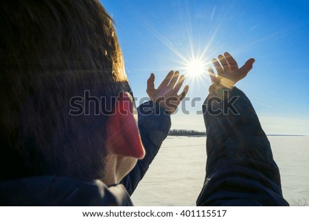 The boy stands on  shore   frozen river and pulled by hand to sun.