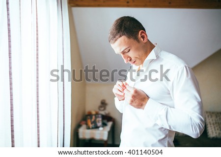 Stylish and handsome groom in waistcoat tying his bow-tie in the morning of the wedding day. Royalty-Free Stock Photo #401140504