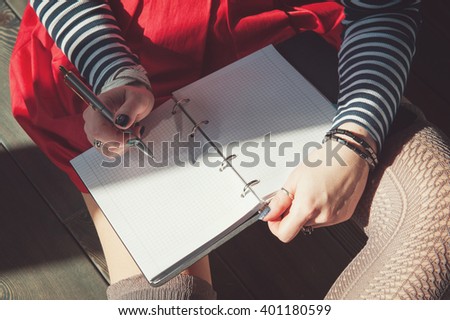 Cozy photo of woman writing in notebook sitting on the floor in sunlight