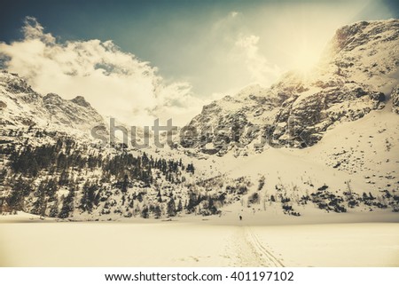 Retro old film style picture of Tatra Mountains against the sun, view from frozen Lake Morskie Oko, Poland.