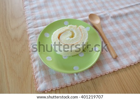 Vanilla roll cake on cute polka dots pastel green plate with wooden dessert spoon on pink plate mat.