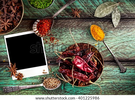 Spices, blank photo frame and dry red chili peppers at wooden green background with spoons nearby