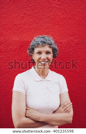 Portrait of attractive middle aged woman with her arms crossed standing against red background. Smiling mature female against red wall.