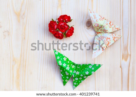 Origami butterfly and red Paper flowers on wood background.