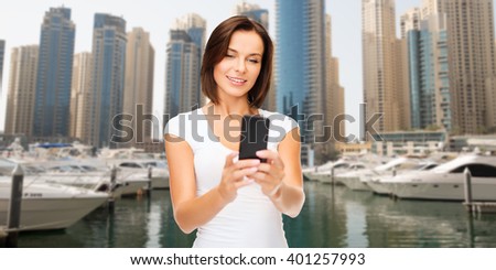 travel, tourism, summer vacation, technology and people - happy young woman taking selfie picture by smartphone over dubai city waterfront and boats background