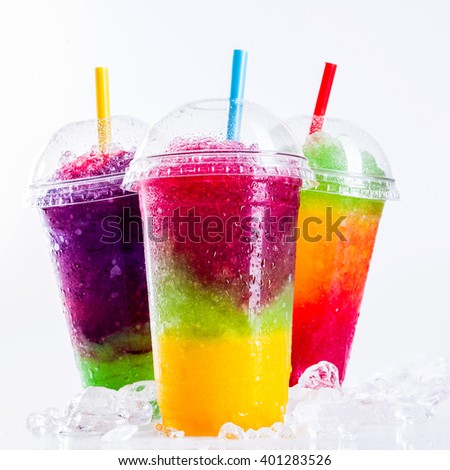 Still Life Close Up of Colorful Rainbow Layered Frozen Fruit Slush Drinks Arranged on Ice Covered White Surface in Plastic Take Away Cups with Drinking Straws - Trio of Refreshing Granitas Royalty-Free Stock Photo #401283526