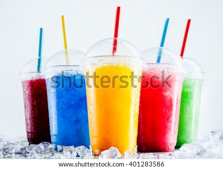Still Life Profile of Frozen Fruit Slush Granita Drinks in Plastic Take Away Cups with Lids and Drinking Straws Chilling on Cold Metal Surface with Scattered Ice Cubes Royalty-Free Stock Photo #401283586