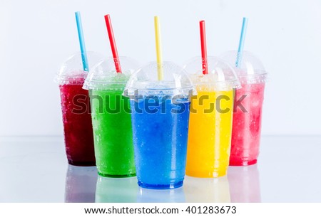Still Life Profile of Frozen Fruit Slush Granita Drinks in Plastic Take Away Cups with Lids and Drinking Straws Arranged on Reflective Surface in front of White Background Royalty-Free Stock Photo #401283673