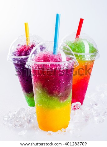 Still Life Close Up of Colorful Rainbow Layered Frozen Fruit Slush Drinks Arranged on Ice Covered White Surface in Plastic Take Away Cups with Drinking Straws - Trio of Refreshing Granitas Royalty-Free Stock Photo #401283709