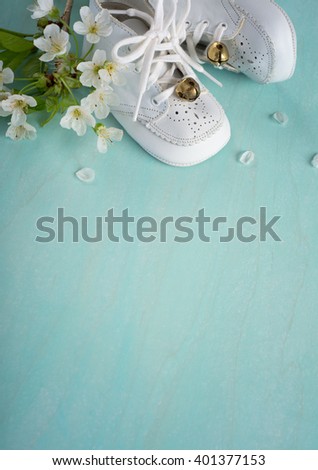 Cute, White Vintage Leather Infant Baby Shoes with spring flowers on Cyan Turquoise Faux Painted, Rustic wood Board Background with room or space for copy, text, your words. Vertical aerial side view