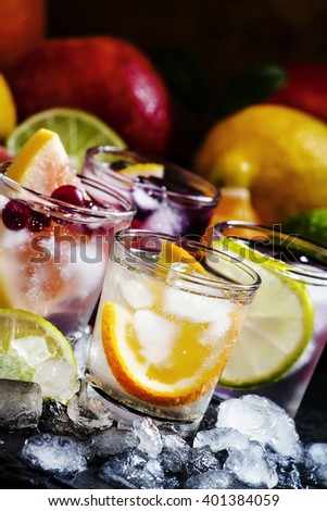 Chilled soft drinks with ice, citrus fruits and berries, black background, selective focus
