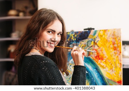 Creative happy painter paints a colorful picture. Closeup of painting process in art workplace. Smiling positive woman painter paints in her studio. 