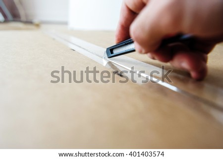 Man cutting with sharp cutter knife a cardboard box to open it before installing furniture Royalty-Free Stock Photo #401403574