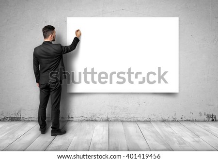 Back view of businessman drawing at white empty canvas on concrete wall