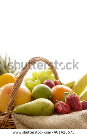 Close up detail of a basket full of fresh bio fruit (banana, apple, pear, grapes, orange, pineapple...) on a light background â??Â� high key photography
