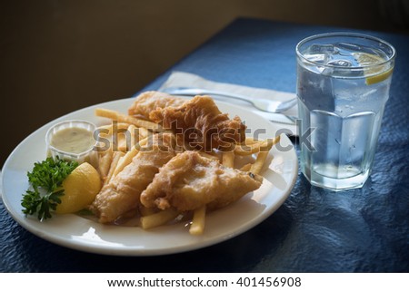 A plate of fried fish, cod or halibut, with french fries or chips with a glass ow water
